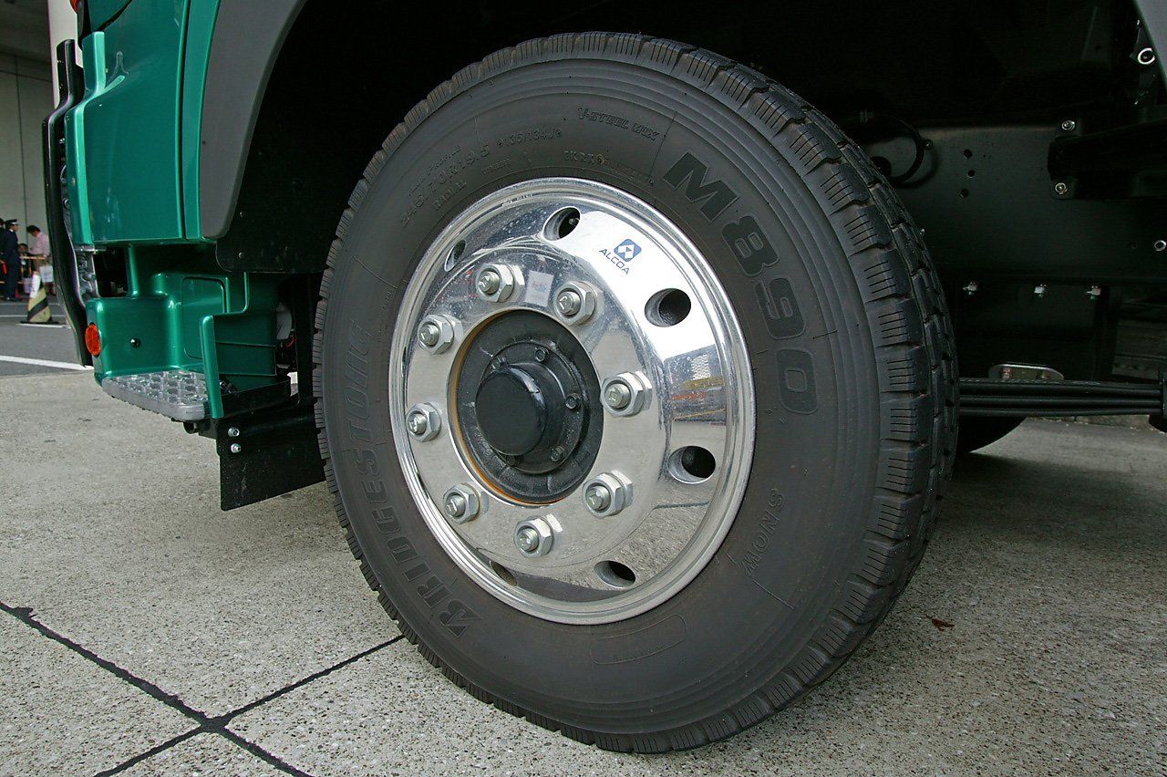 Truck tire on a green truck, featuring a silver rim with bolts and black rubber.
