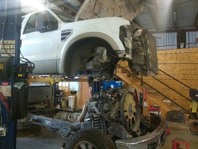 White truck being repaired in a garage. The engine is visible and exposed.