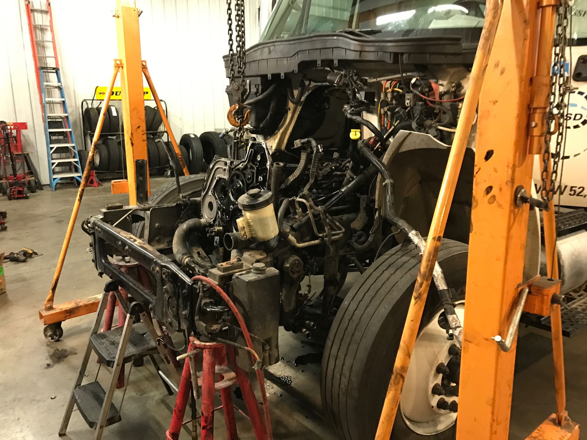 Truck with engine removed, suspended by a hoist.  Workshop setting, tools visible.