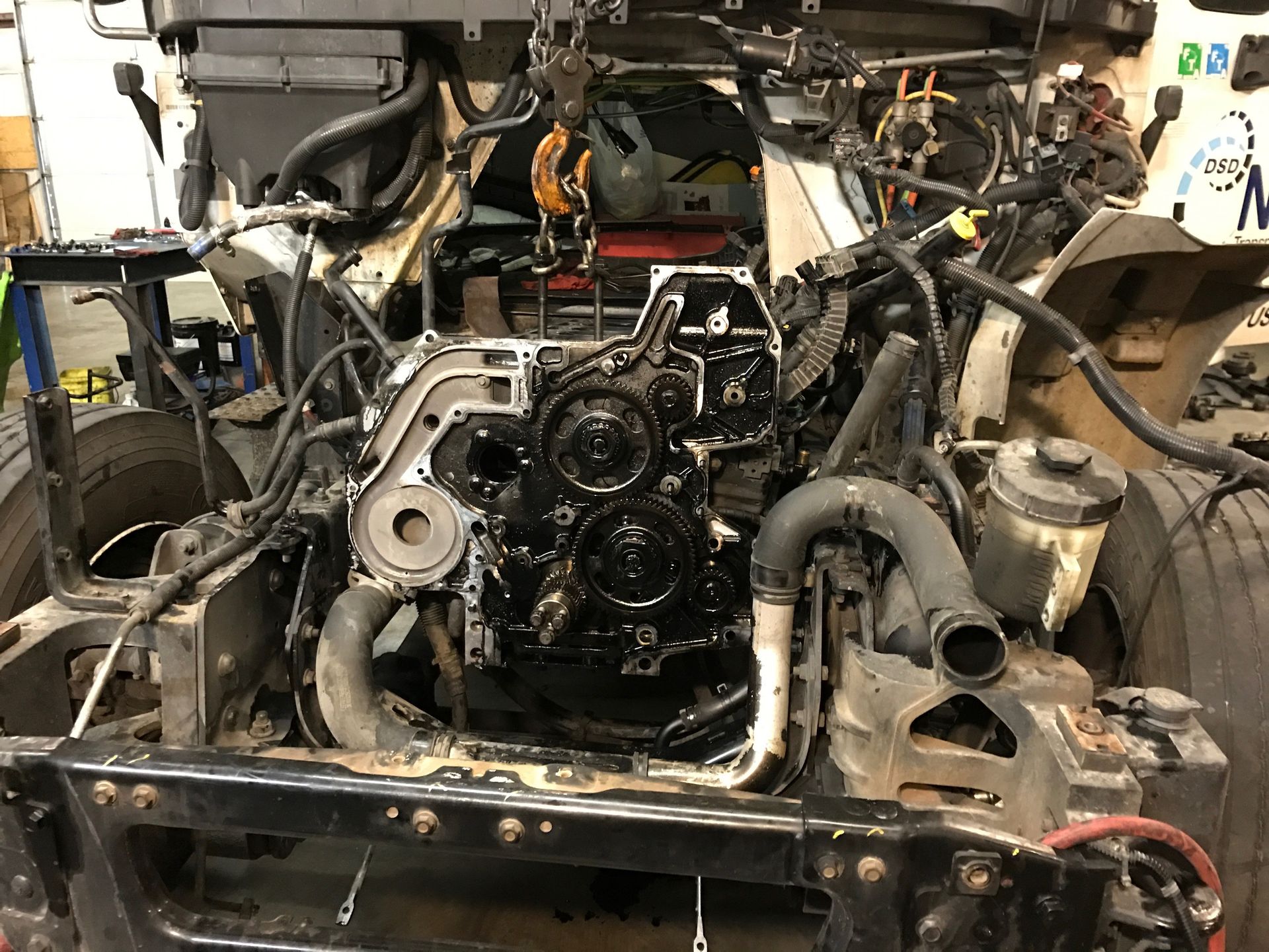 Black engine in a partially disassembled truck, viewed from the front. Wiring and hoses are visible.