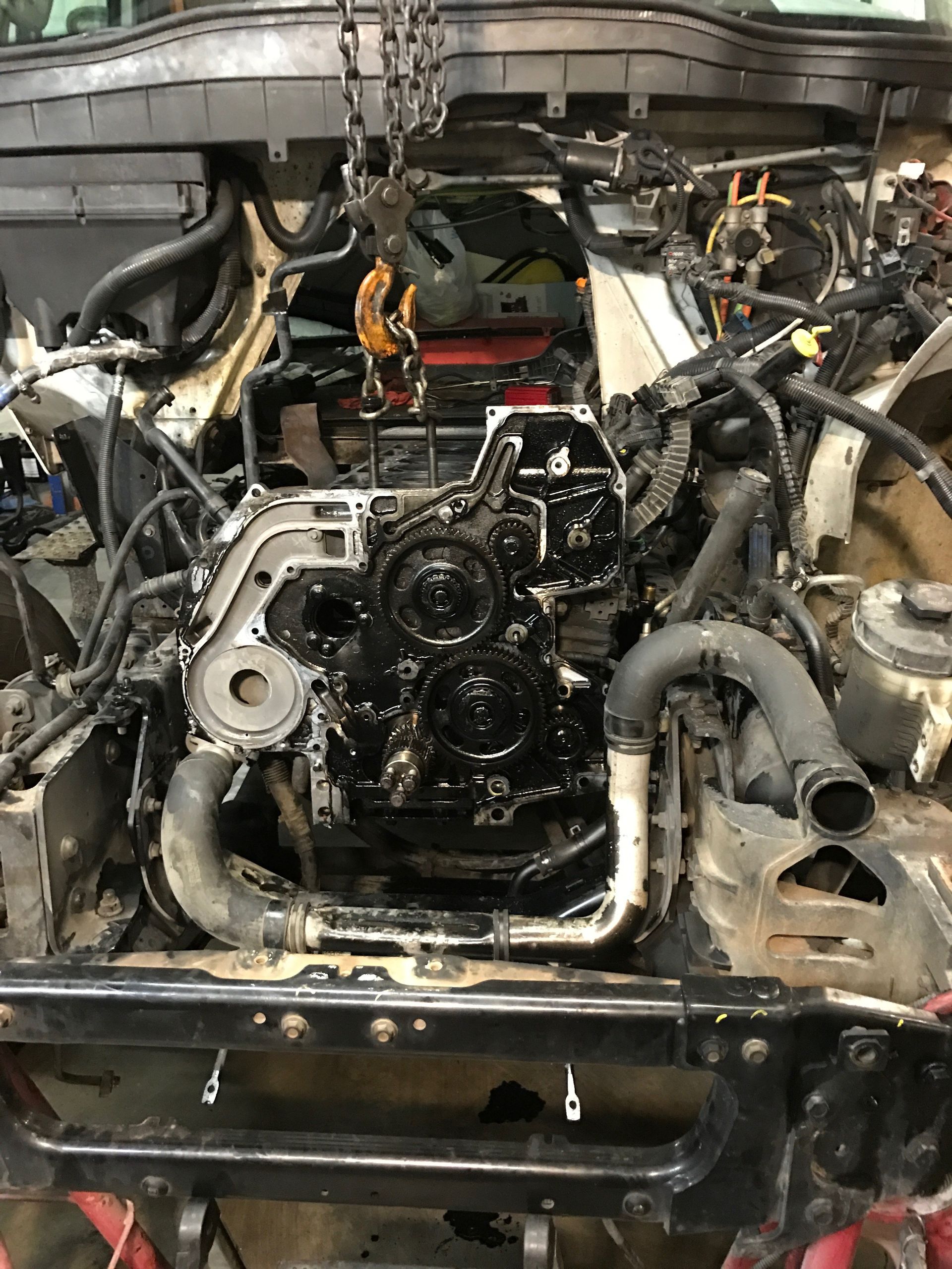 A black engine is being lifted out of a vehicle by a chain in a garage.