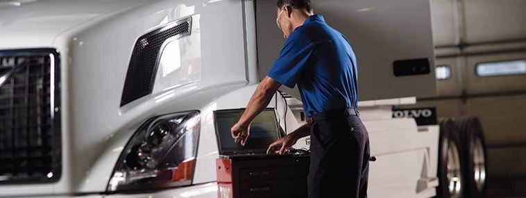 Mechanic using a laptop to diagnose a semi-truck in a garage.
