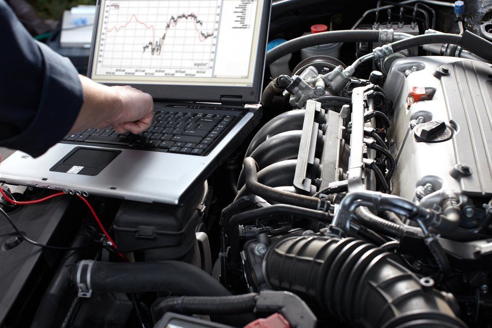 Mechanic using a laptop to diagnose a car engine.  Gauges and engine components visible.