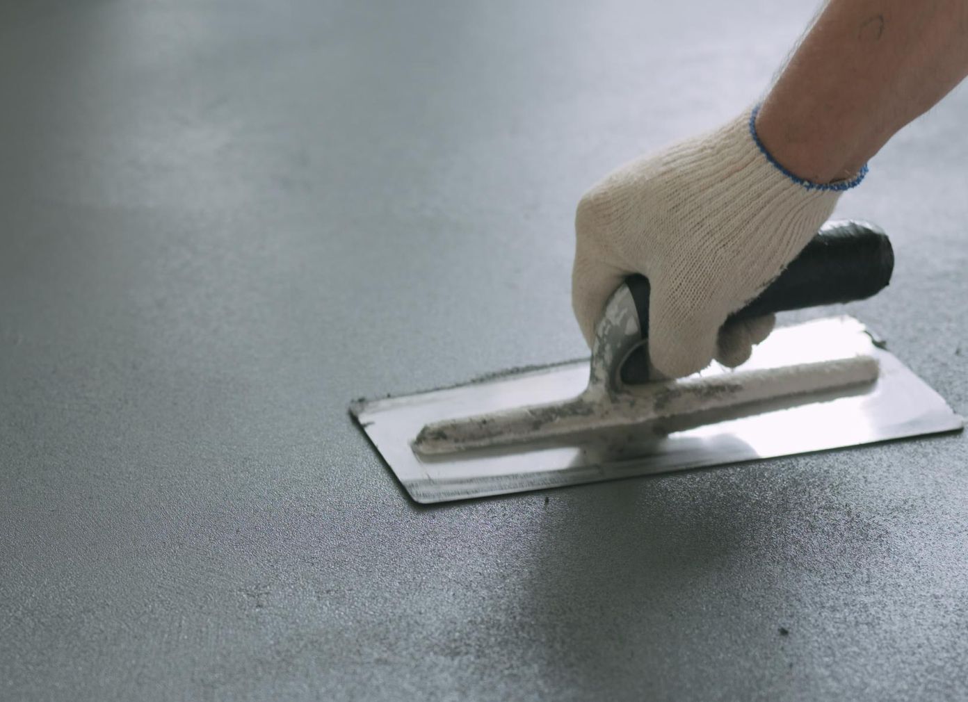 A person is using a trowel on a concrete floor.