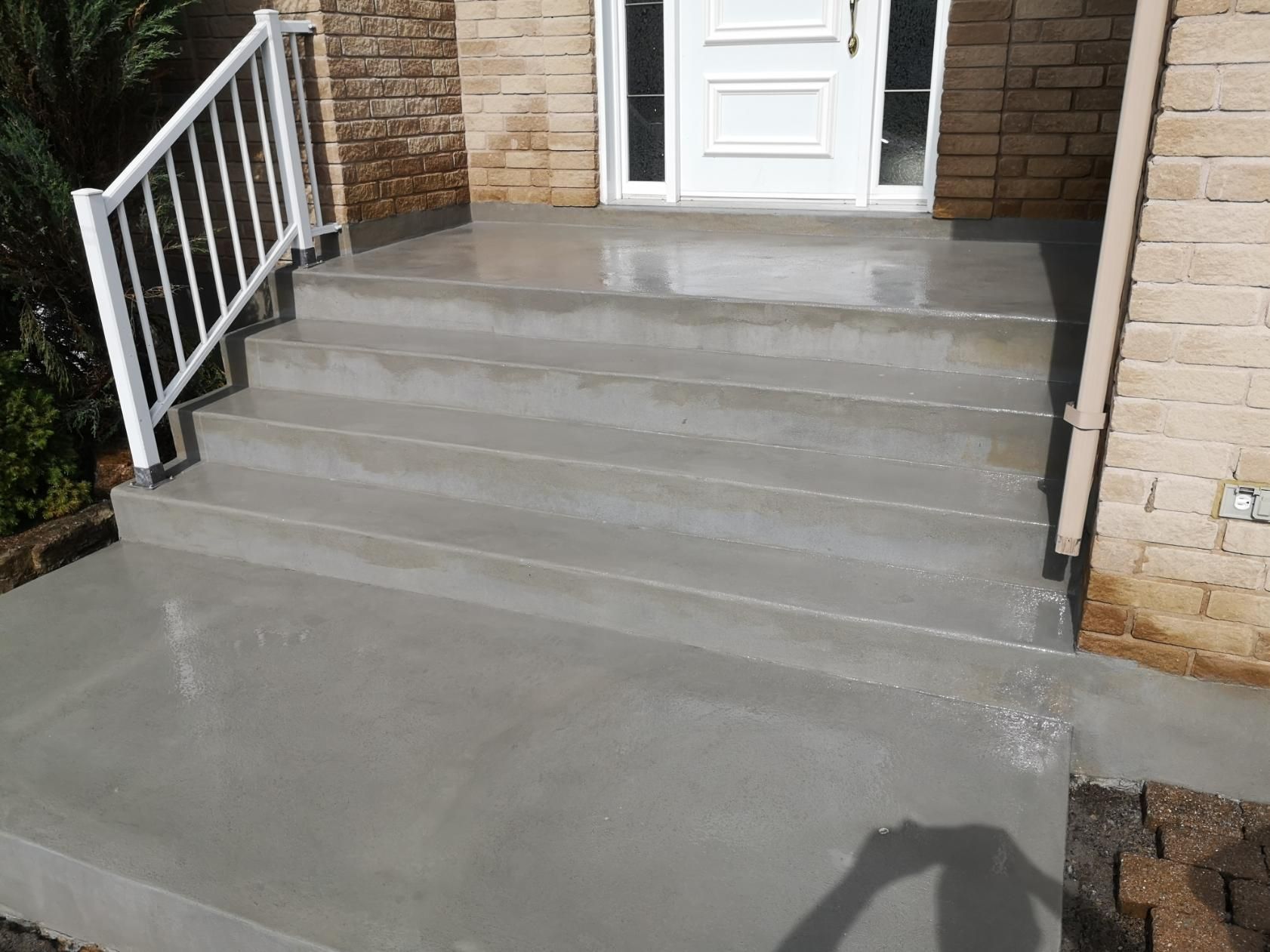 A set of concrete steps leading up to a house with a white railing.