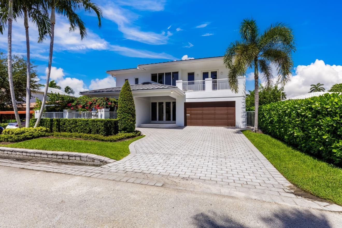 A large white house with a driveway and palm trees in front of it.