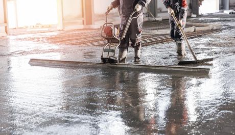 Two men are cleaning a concrete floor with a vacuum cleaner.