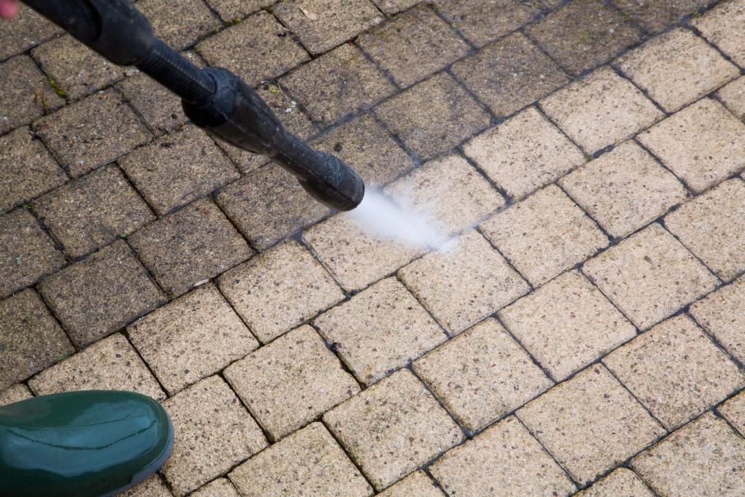 A person is using a high pressure washer to clean a brick walkway.