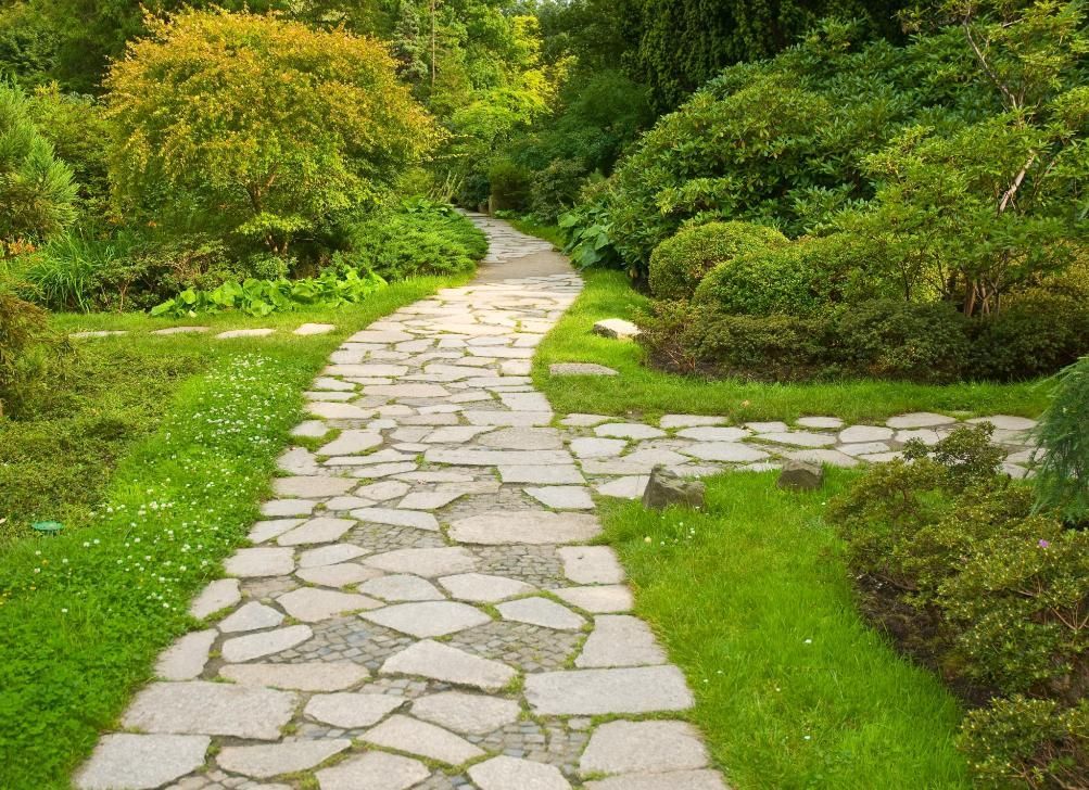 A stone path in a park surrounded by grass and trees.