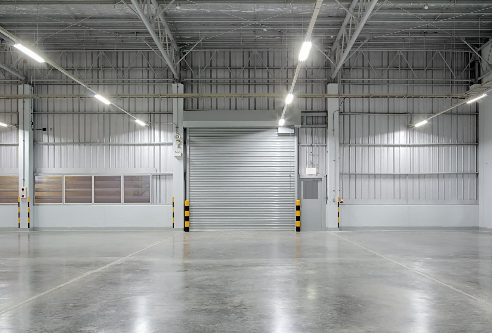 An empty warehouse with a rolling door and a concrete floor.
