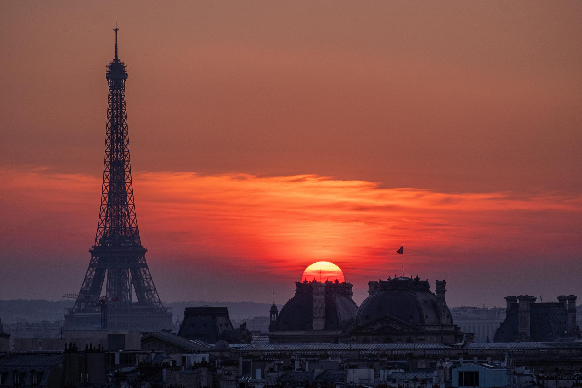 Silhouette de la tour Eiffel au coucher du soleil sur Paris, avec un ciel rouge-orangé et les toits de la ville dans l'ombre