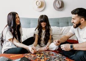 Family of three laughing, doing a puzzle on a bed.