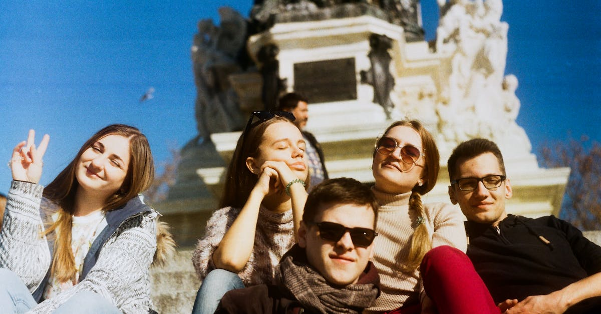 Cinq amis posent et sourient à l'extérieur, près d'un monument blanc, sous un ciel bleu.