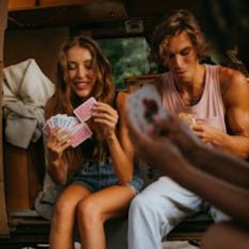 Two people playing cards, smiling. Outdoor setting, natural light.