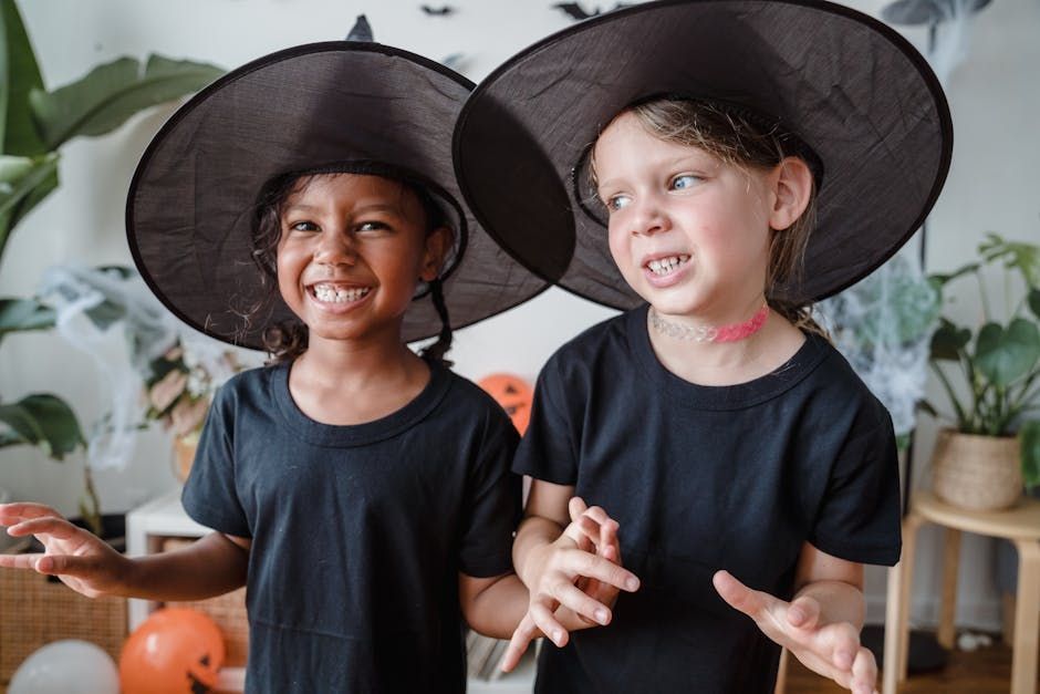 Deux enfants souriants, coiffés de chapeaux de sorcière noirs et vêtus de chemises, dans une chambre décorée pour Halloween.
