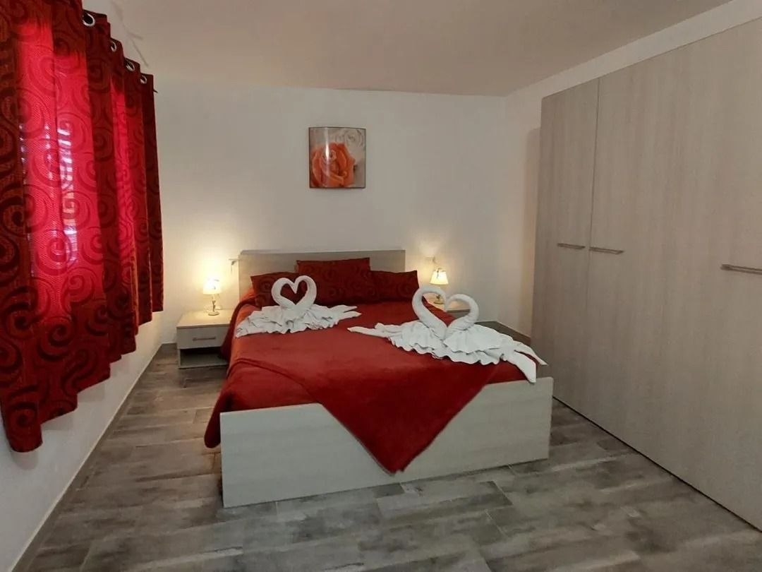 Camera da letto con biancheria da letto rossa, tende e asciugamani decorati con cigni. Pavimento grigio e armadio bianco.