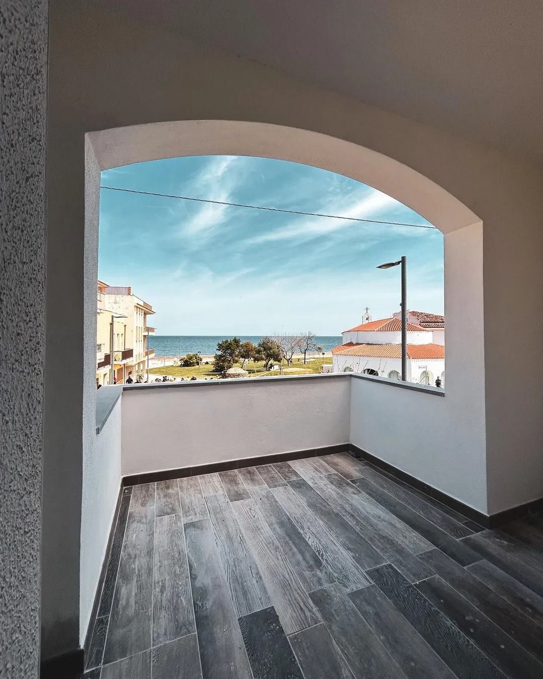 Balcone con apertura ad arco che si affaccia sulla spiaggia e sulla città sotto un cielo azzurro.