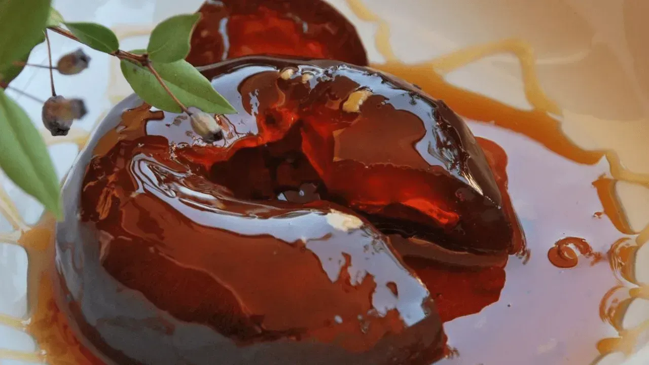 Mele cotogne candite in uno sciroppo marrone, guarnite con un rametto di foglie verdi e bacche.