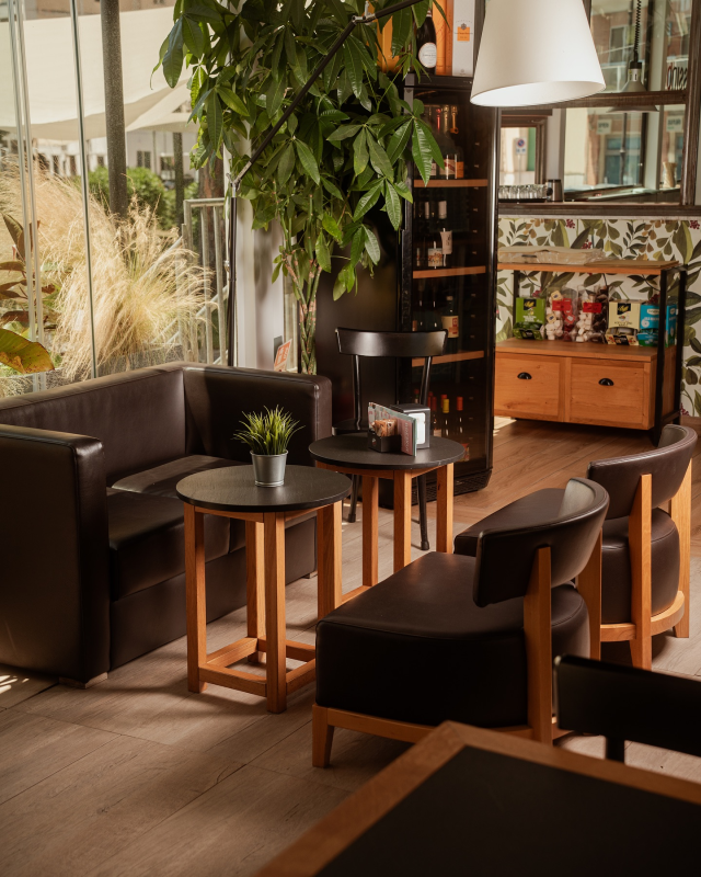 Un'area salotto con mobili in pelle marrone, tavolini e una pianta. Sullo sfondo, un bar con liquori.