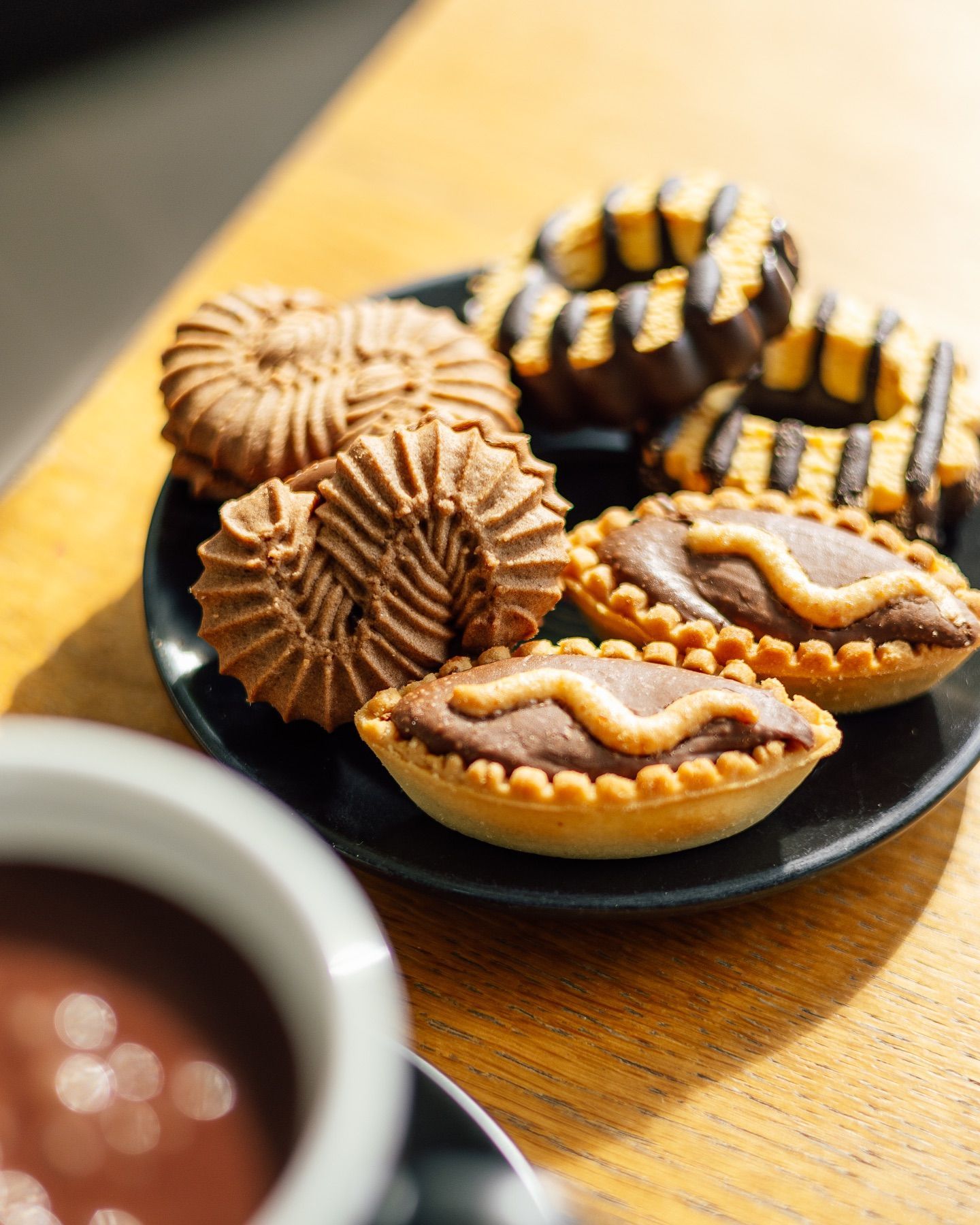 Piatto di biscotti e crostate su un tavolo di legno, accanto a una tazza di cioccolata calda.