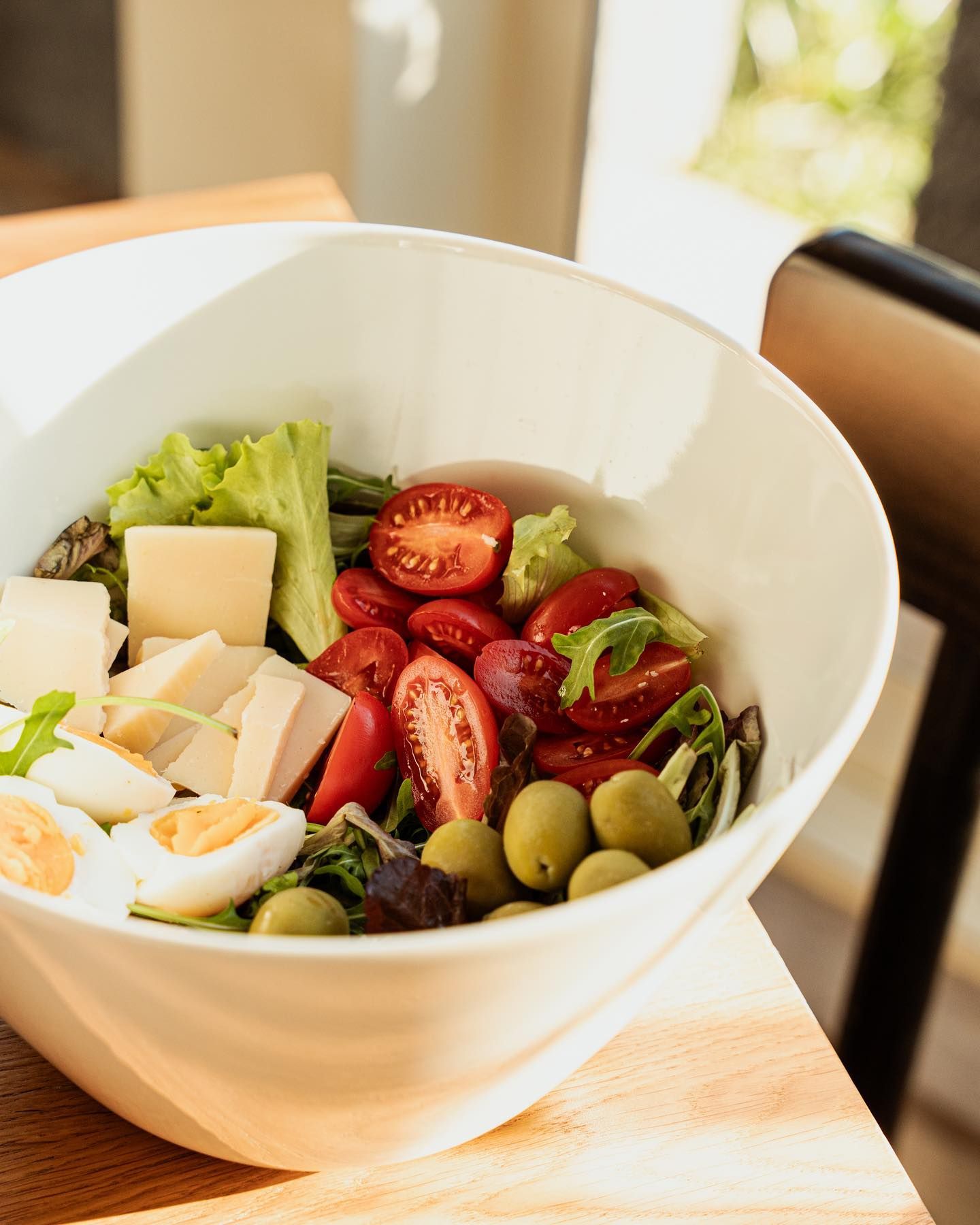 Insalatiera con pomodori, olive, formaggio e uova sode su un tavolo di legno.