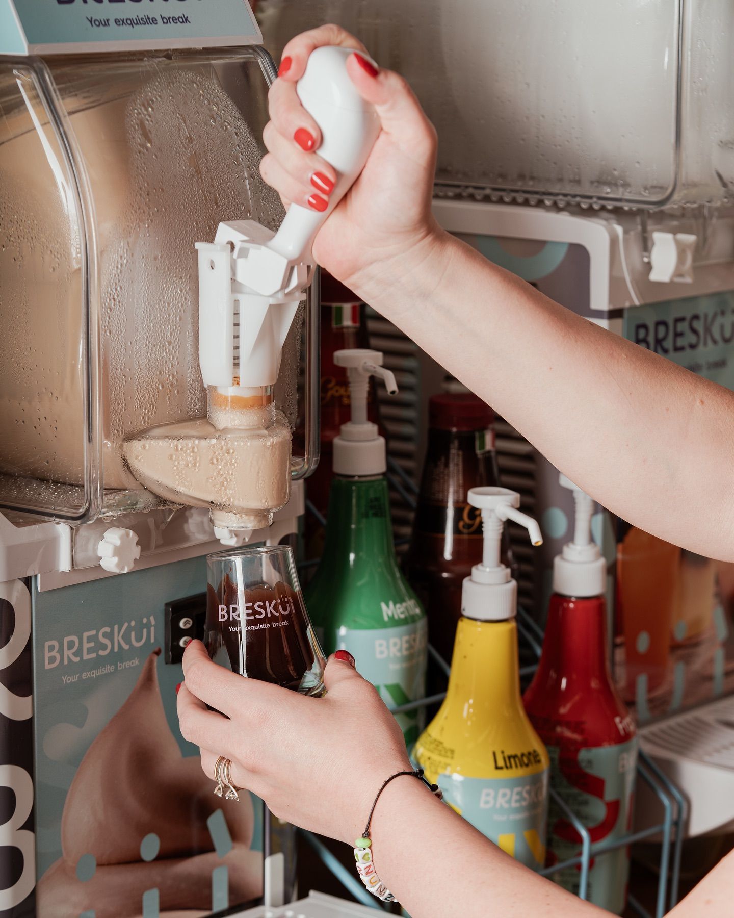 Persona che eroga un liquido scuro da un distributore automatico, con altri aromi sullo sfondo.