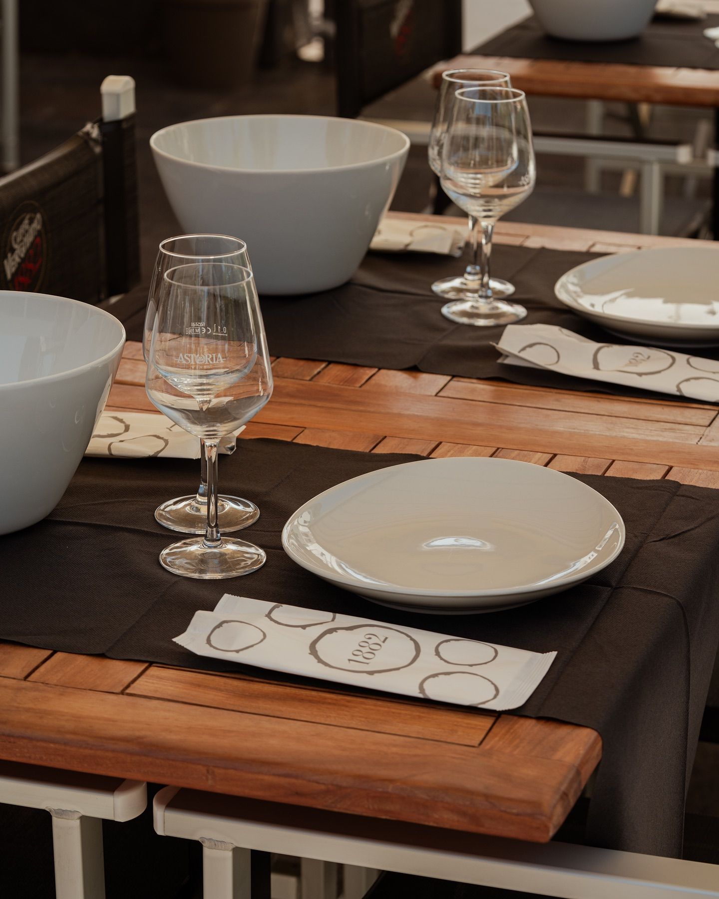 Tavolo del ristorante apparecchiato con piatti bianchi, ciotole e bicchieri da vino.