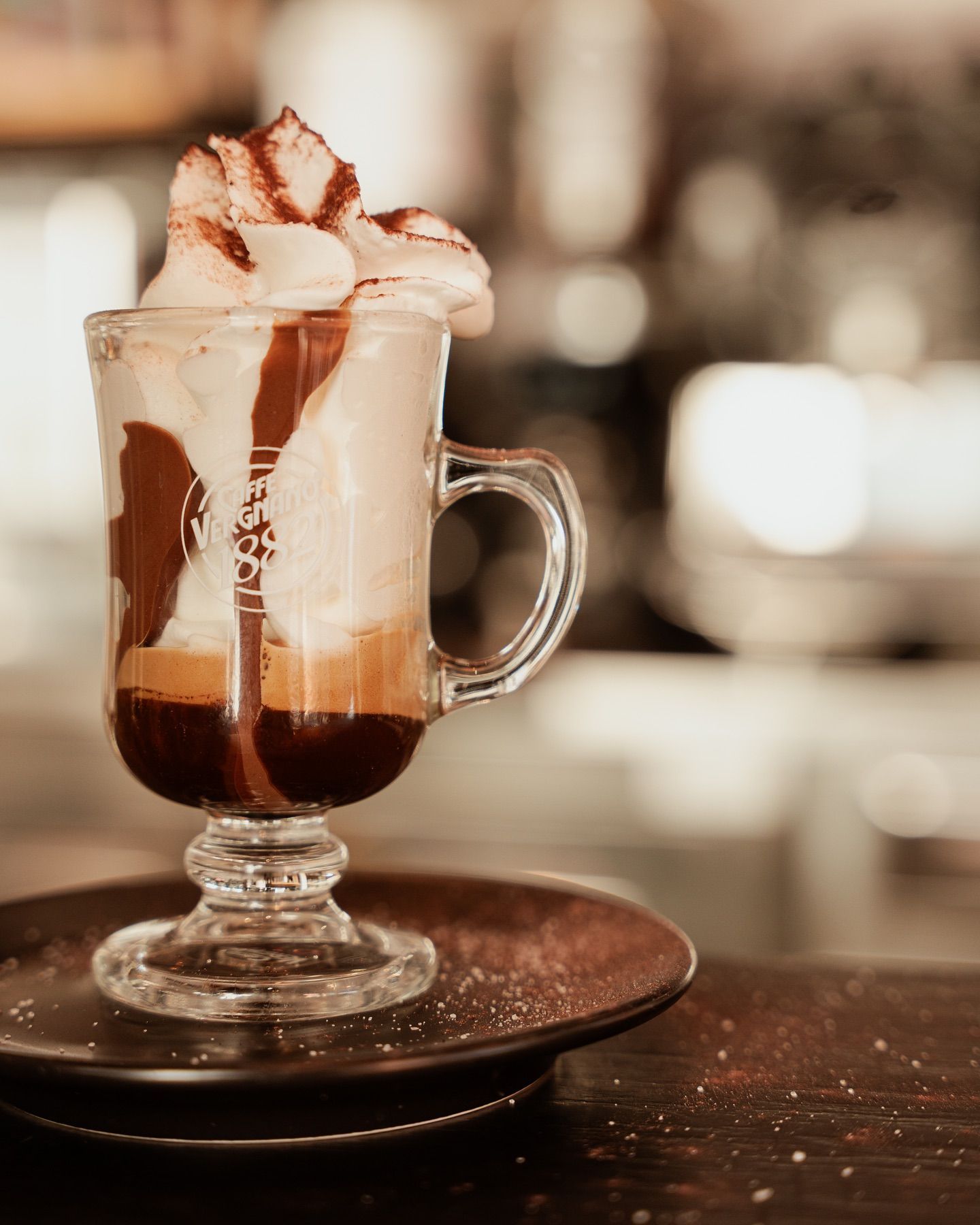 Bevanda al caffè con panna montata e gocce di cioccolato in una tazza di vetro, su un piatto.