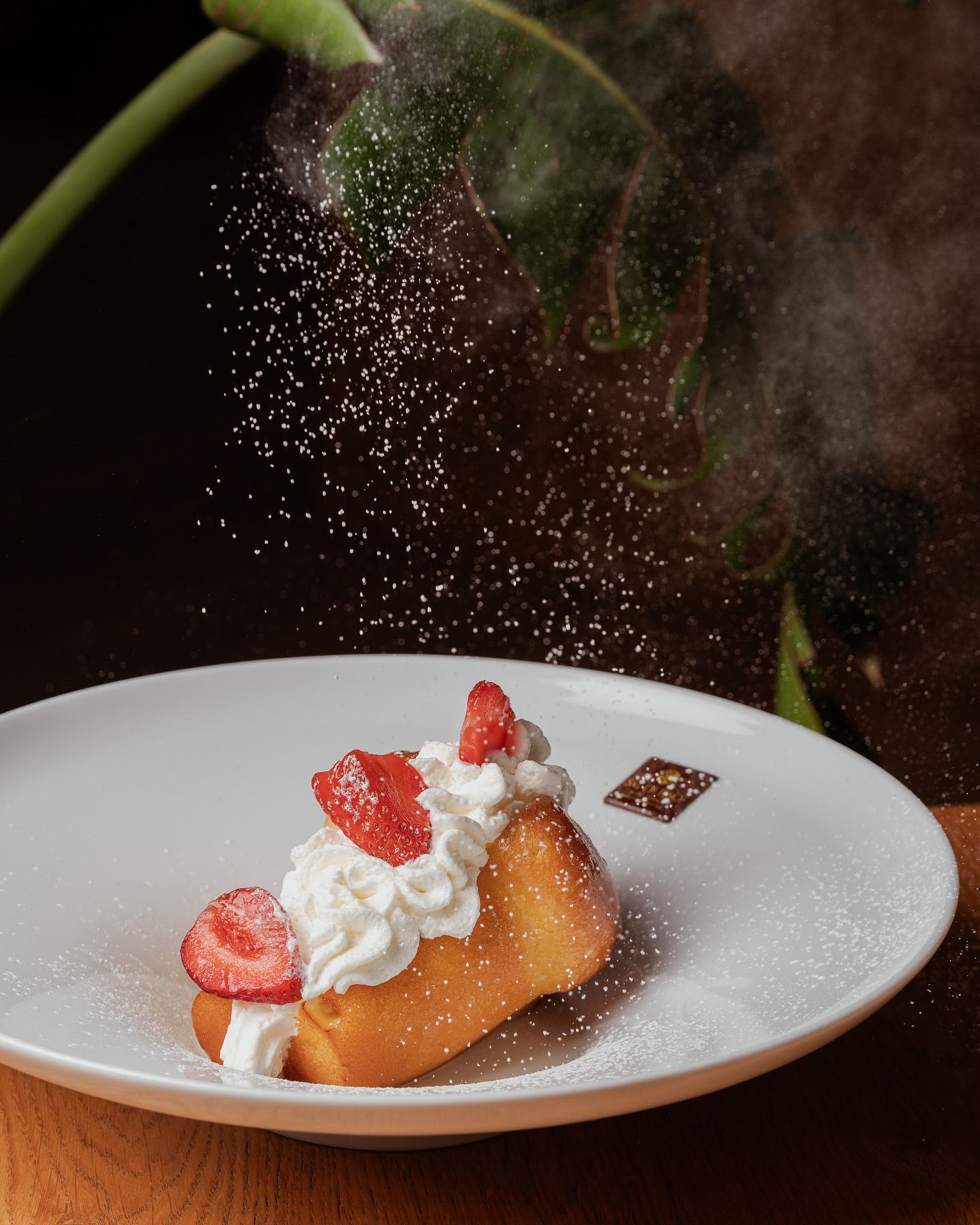 Pasta sfoglia guarnita con panna montata e fragole, spolverata con zucchero a velo, su un piatto bianco.