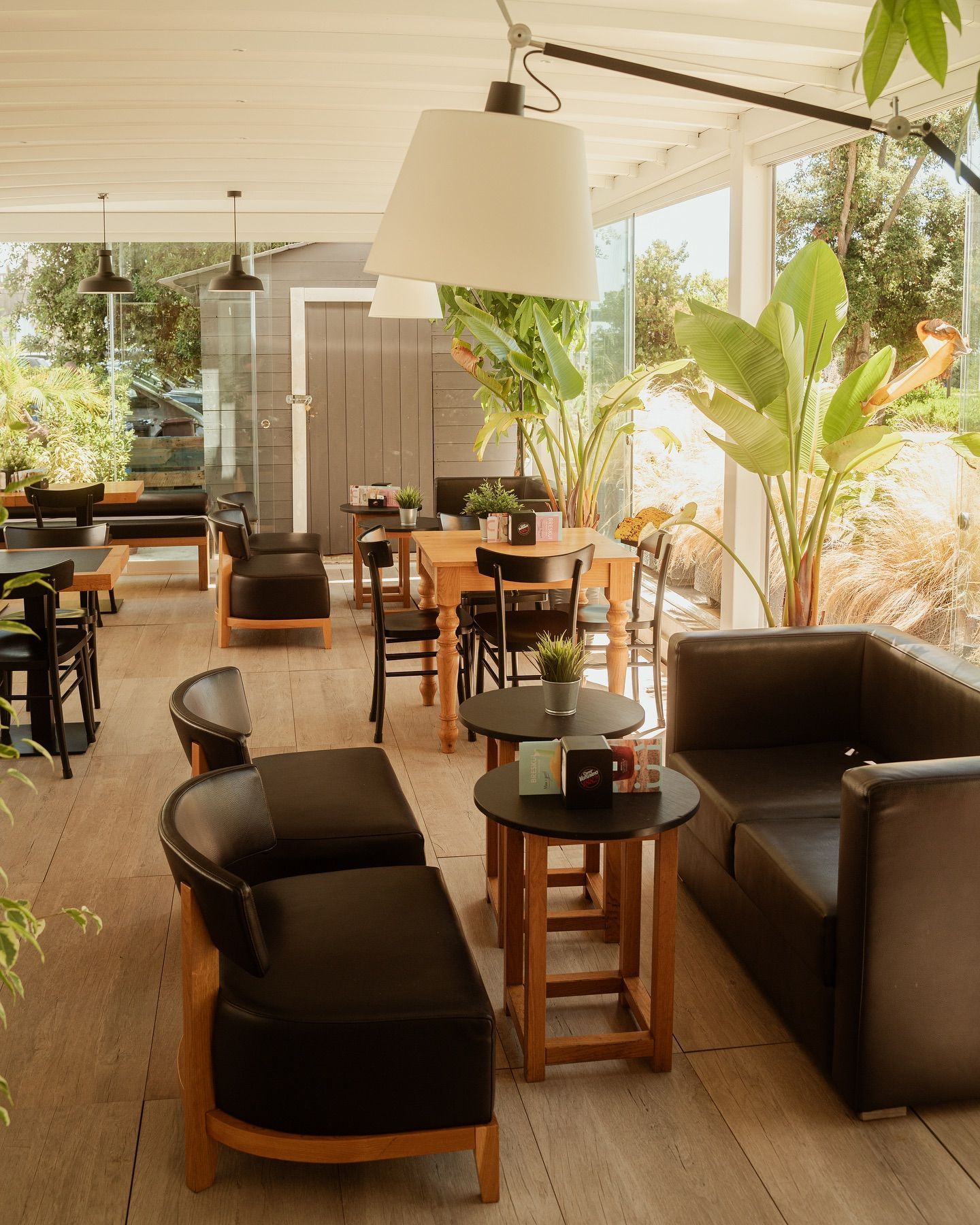 Caffetteria interna con sedute in pelle nera, tavoli in legno e ampie finestre con vista sul verde.