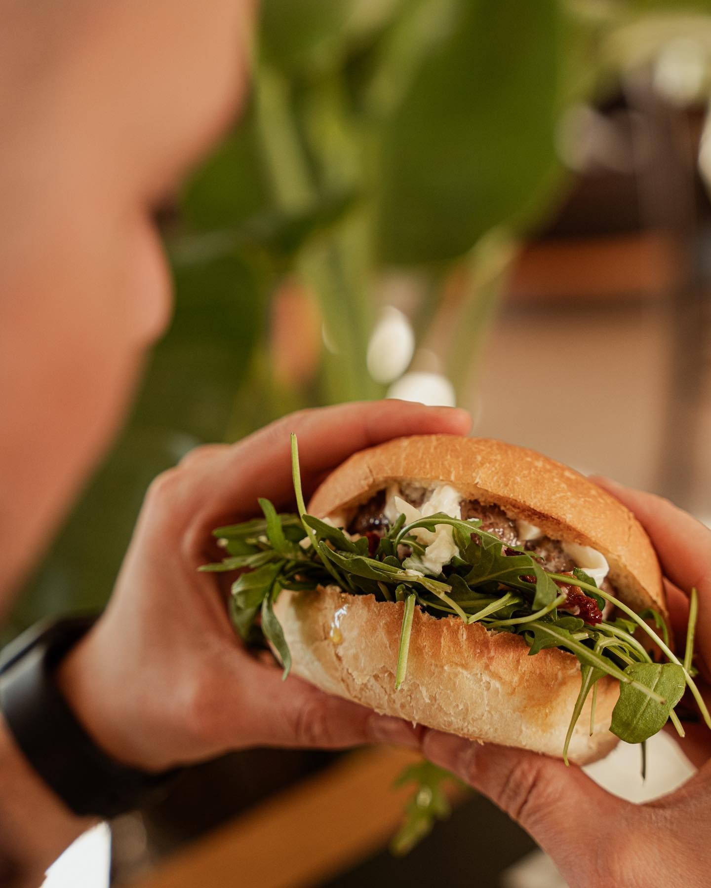 Persona che tiene in mano un panino con la rucola, probabilmente in procinto di addentarlo.