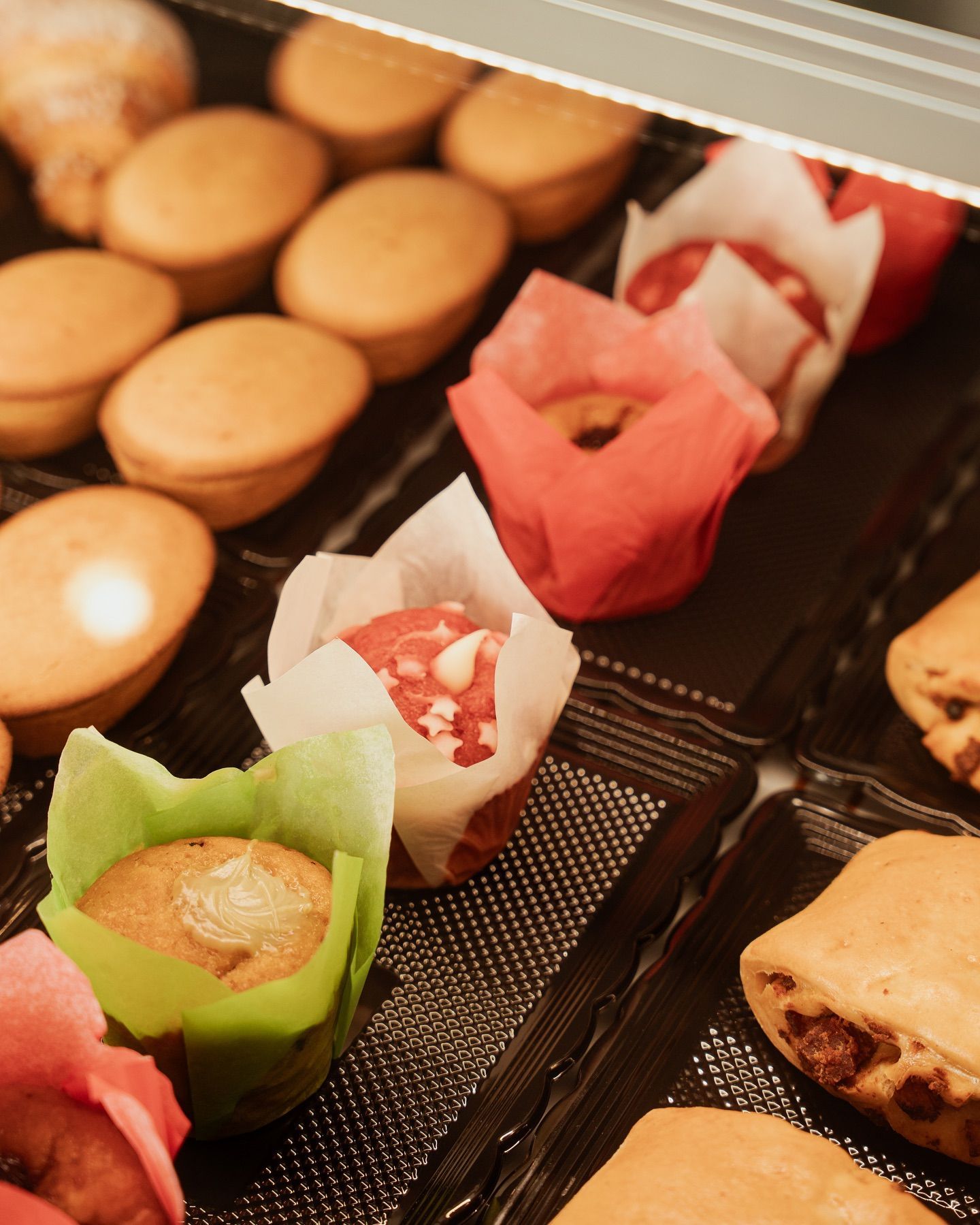 Primo piano di una vetrina di pasticceria con muffin e prodotti da forno in involucri colorati.