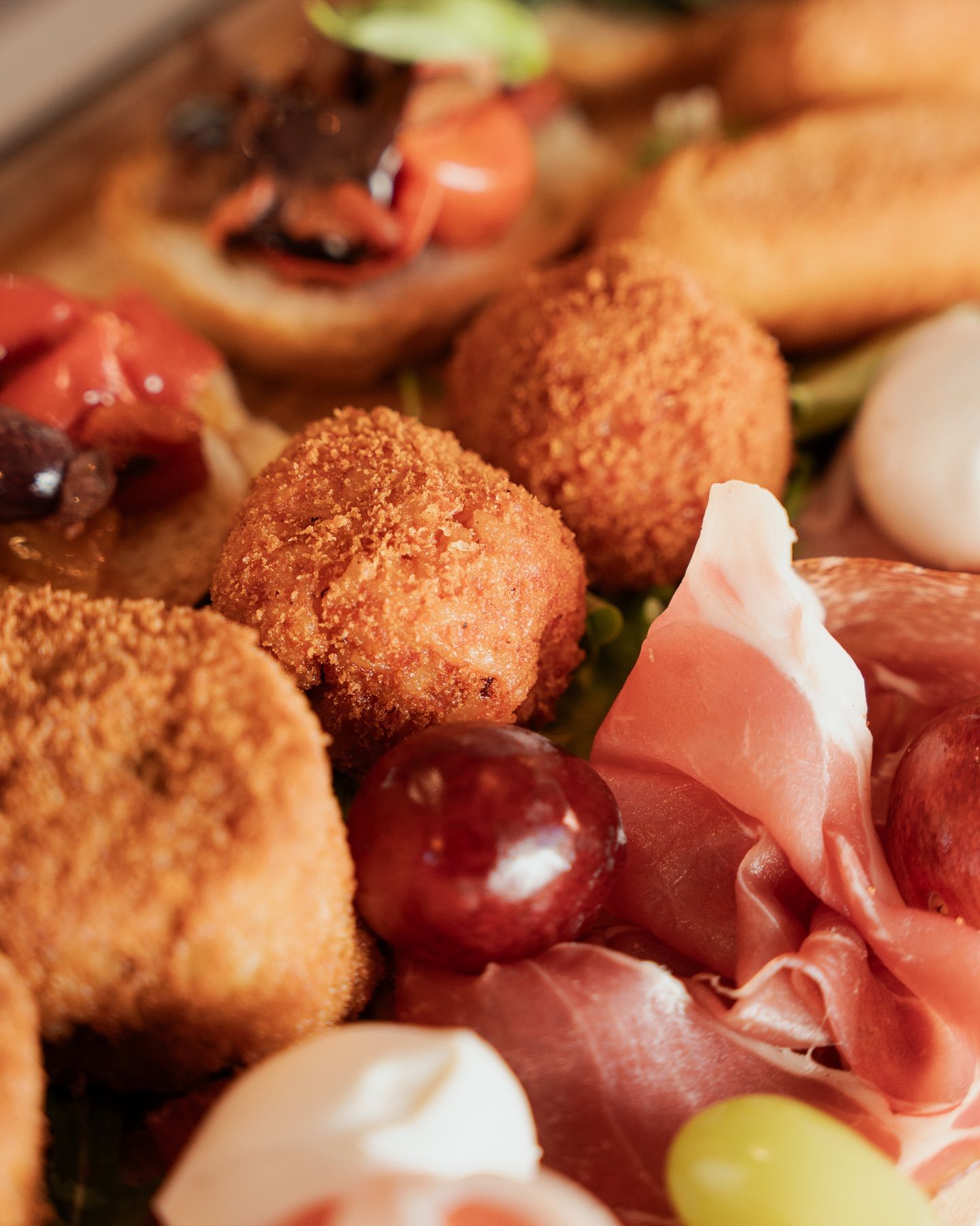 Primo piano di un tagliere di salumi con polpette fritte, carne affettata, uva e altri antipasti.