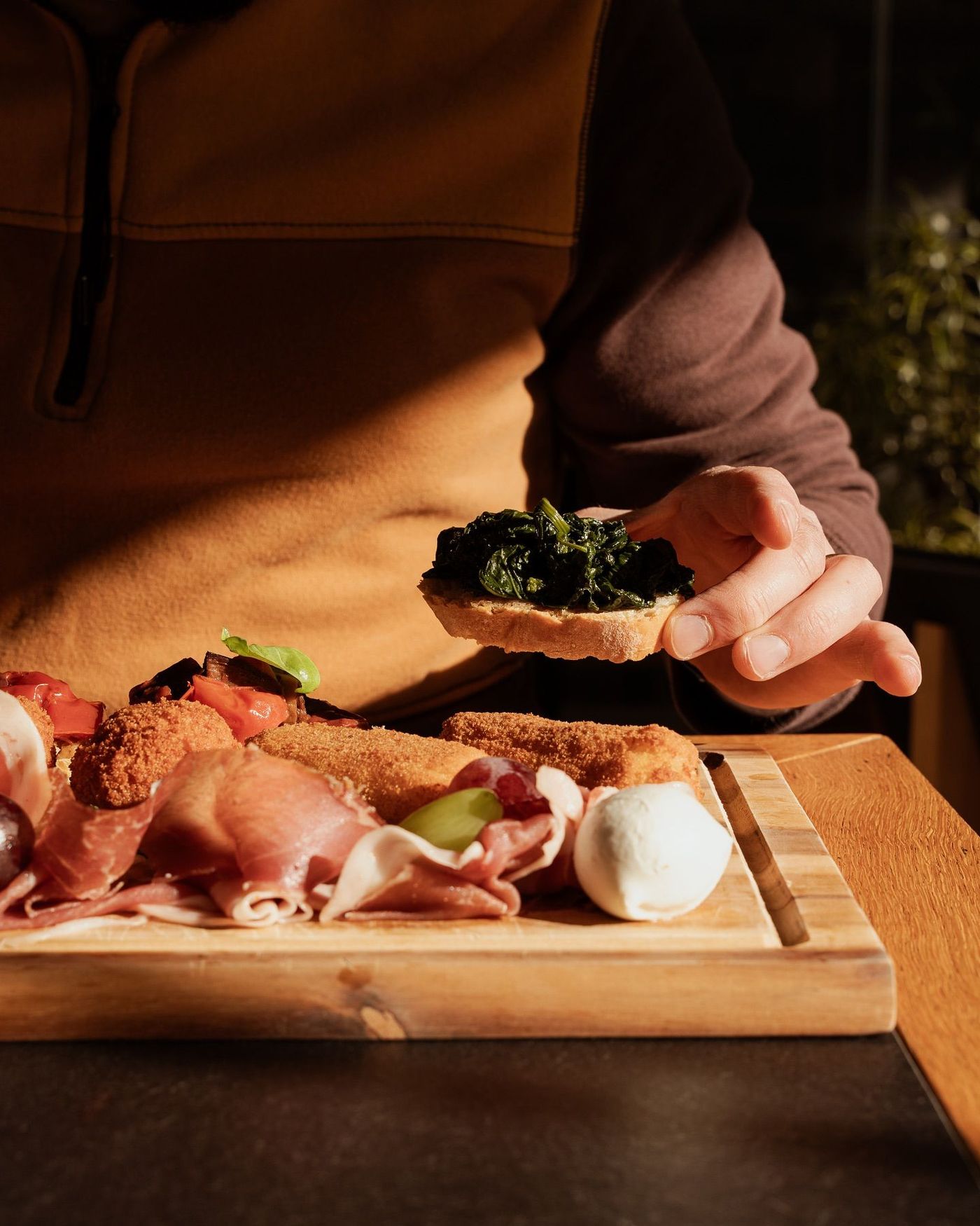 Persona che tiene in mano una fetta di pane condita con verdure sopra un tagliere di legno per salumi.