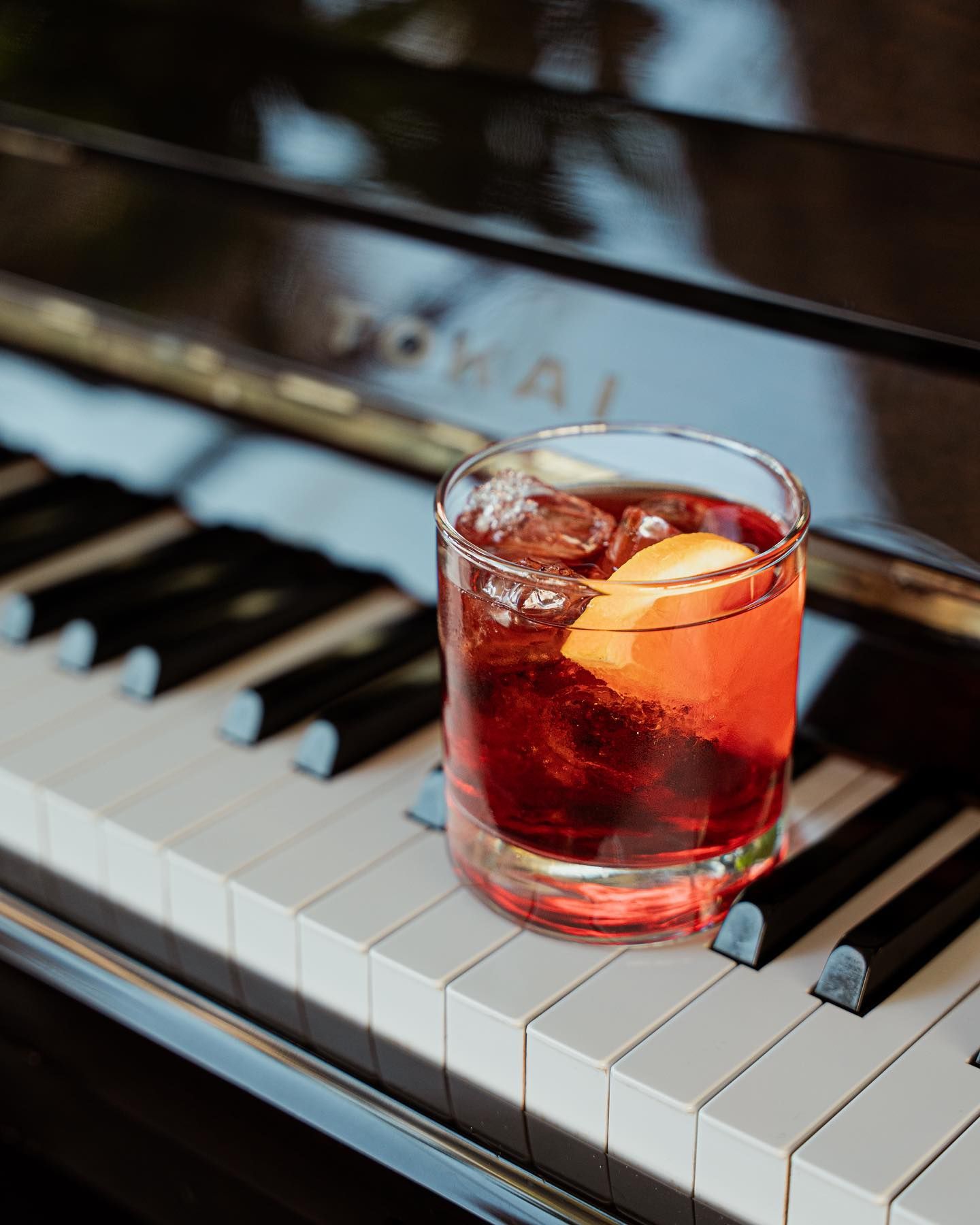 Cocktail in un bicchiere con ghiaccio e una scorza d'arancia sui tasti del pianoforte.