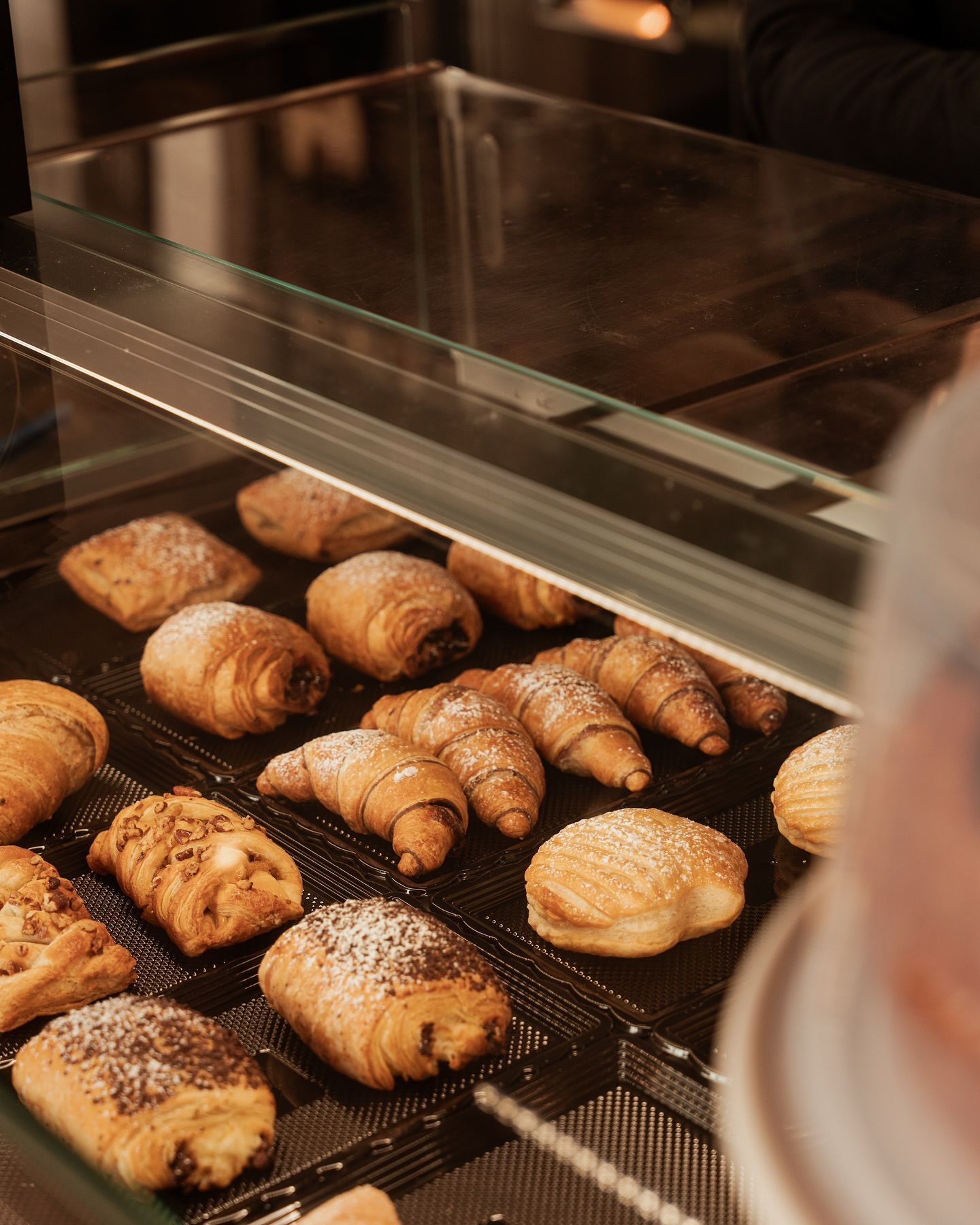 Pasticcini esposti in una teca di vetro, tra cui croissant e panini, spolverati con zucchero a velo.