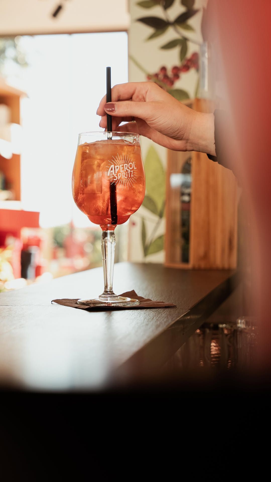 Mescolare a mano un cocktail in un bicchiere con stelo e una cannuccia nera su un bancone.