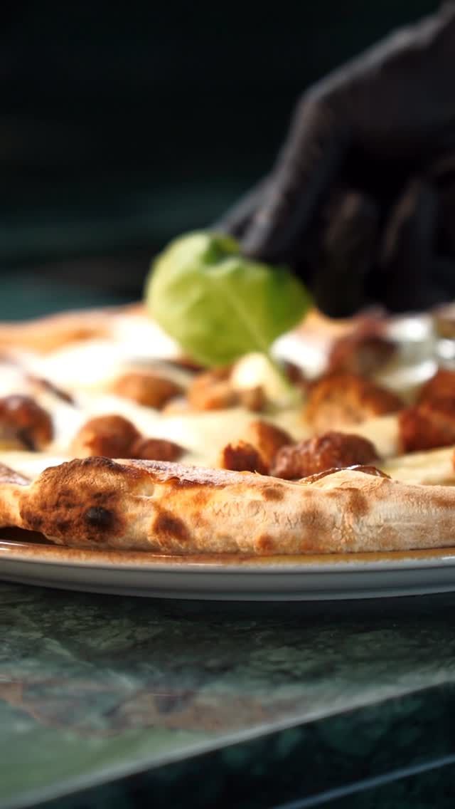 Pizza con formaggio e funghi, una mano guantata depone il basilico.