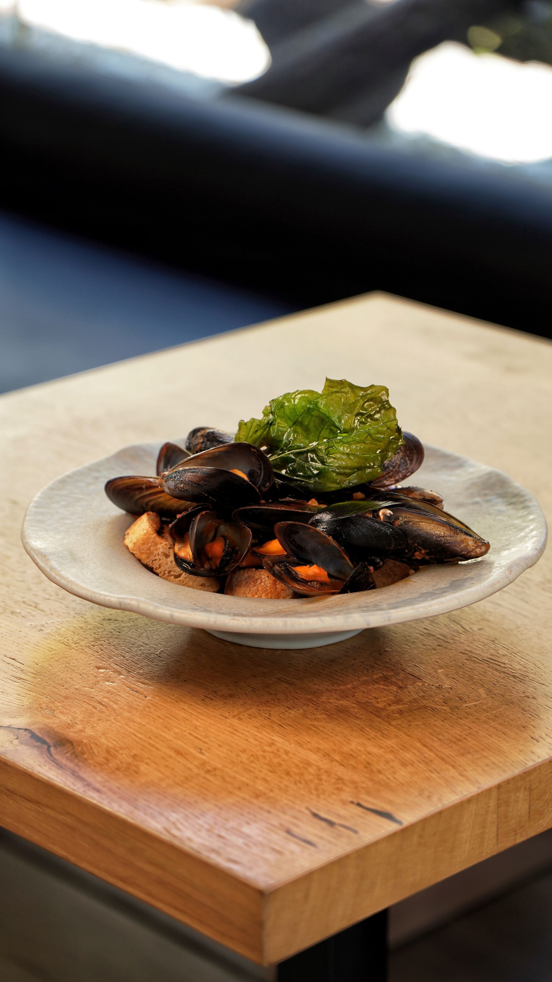 Cozze in salsa verde su un piatto sopra un tavolo di legno. La luce del sole filtra attraverso una finestra.