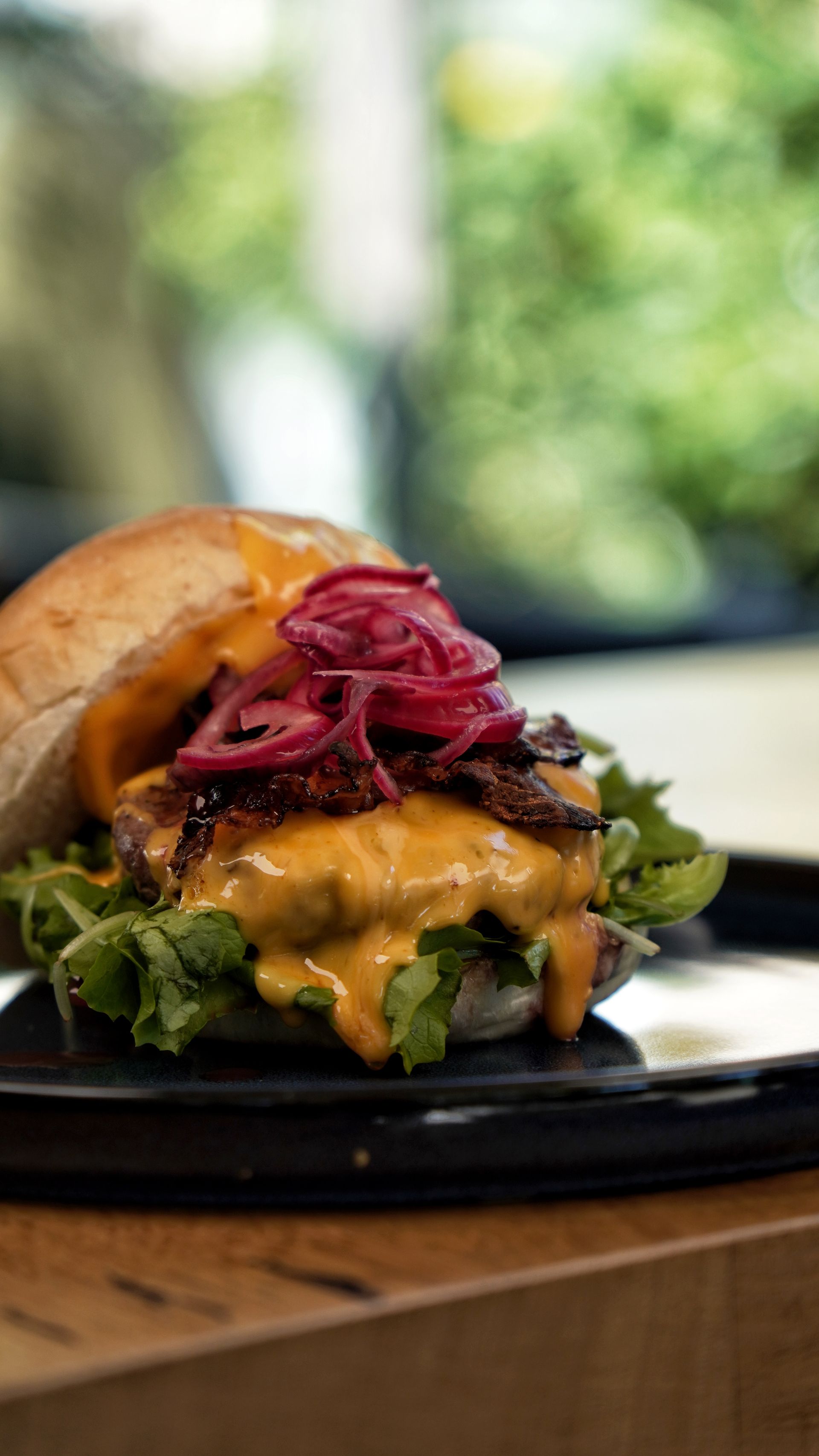 Hamburger con cipolle sottaceto e salsa su un piatto nero, su uno sfondo verde sfocato.
