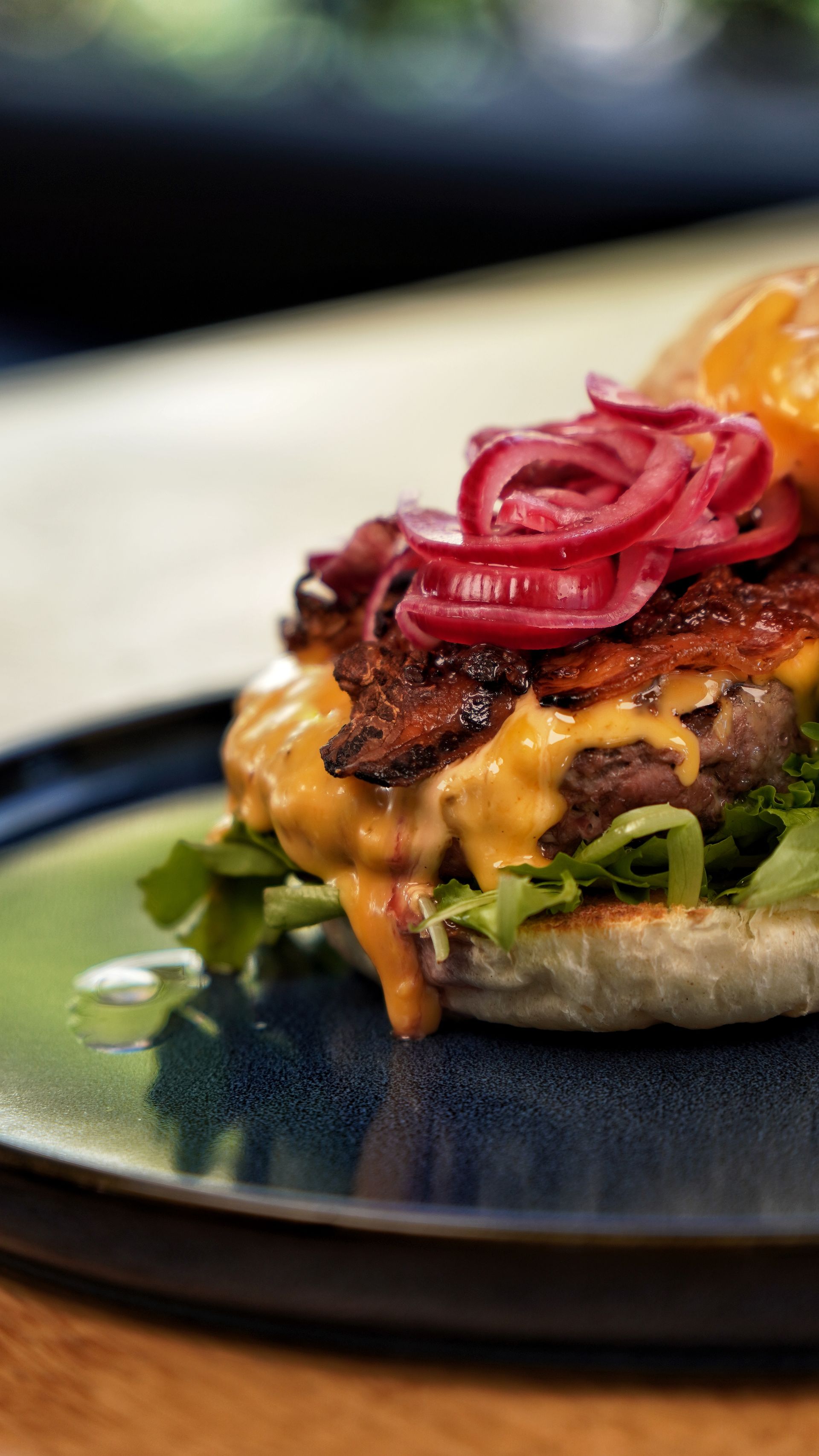 Hamburger su un piatto blu, guarnito con cipolle rosse e salsa, primo piano.