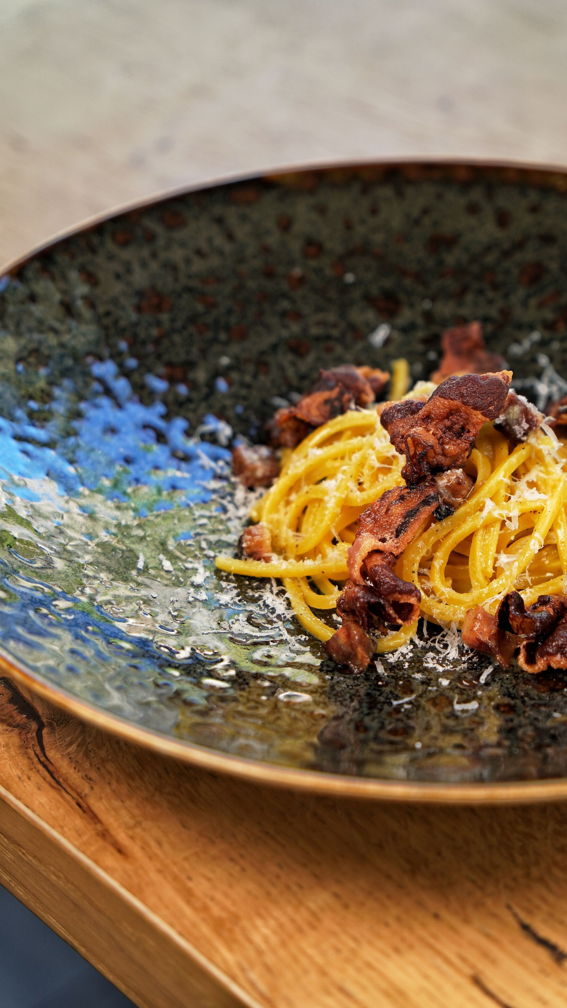 Spaghetti alla carbonara con funghi su un rustico piatto blu scuro, appoggiato su un tavolo di legno.