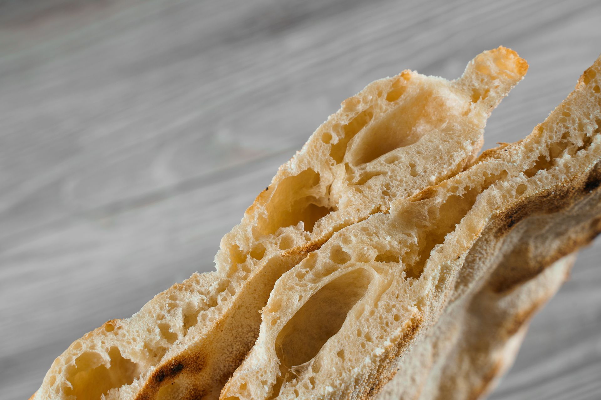 Primo piano di un pane piatto spezzato, che mostra l'interno arioso con buchi visibili e una crosta dorata.