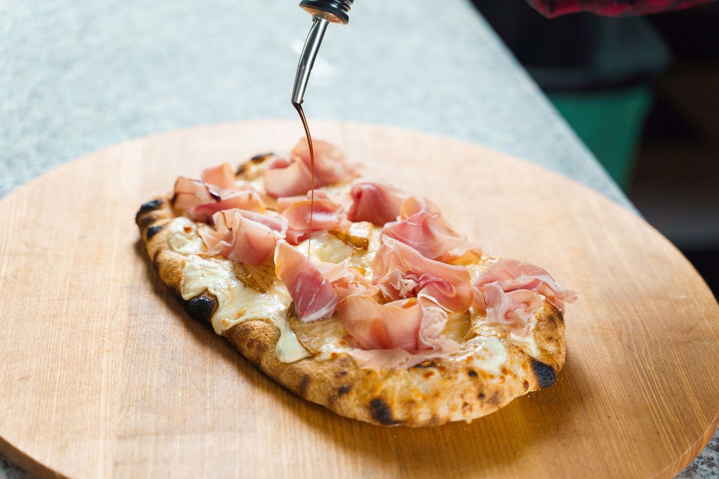 Pizza piatta con prosciutto e formaggio, condita con una salsa scura.