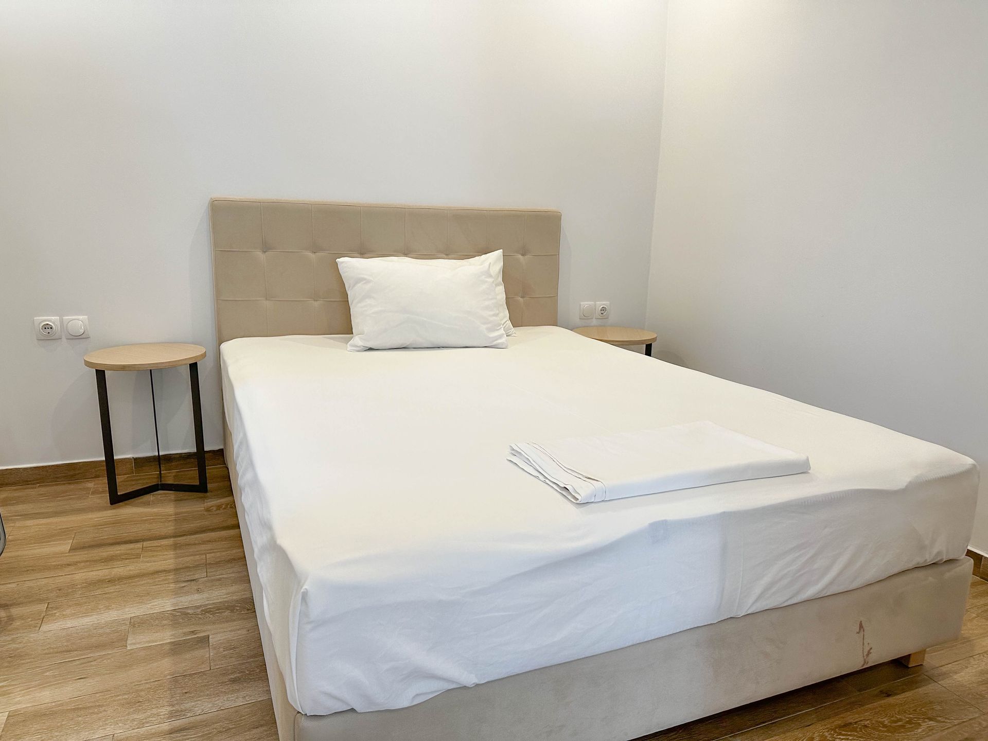 Bedroom with a bed, nightstands, and a folded towel. White walls and neutral colors.
