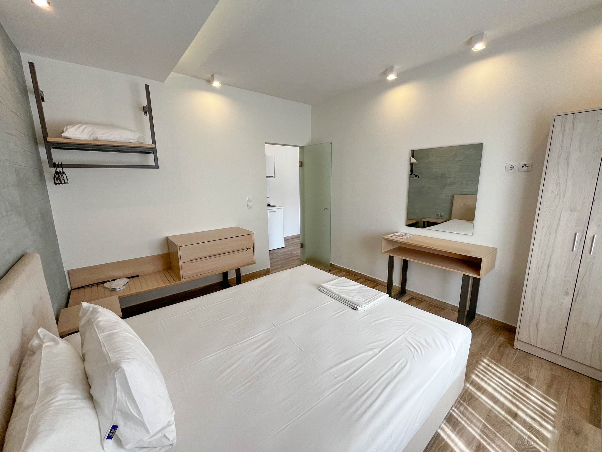 Bedroom with a bed, dresser, and nightstand on a hardwood floor. Light colors dominate the space.