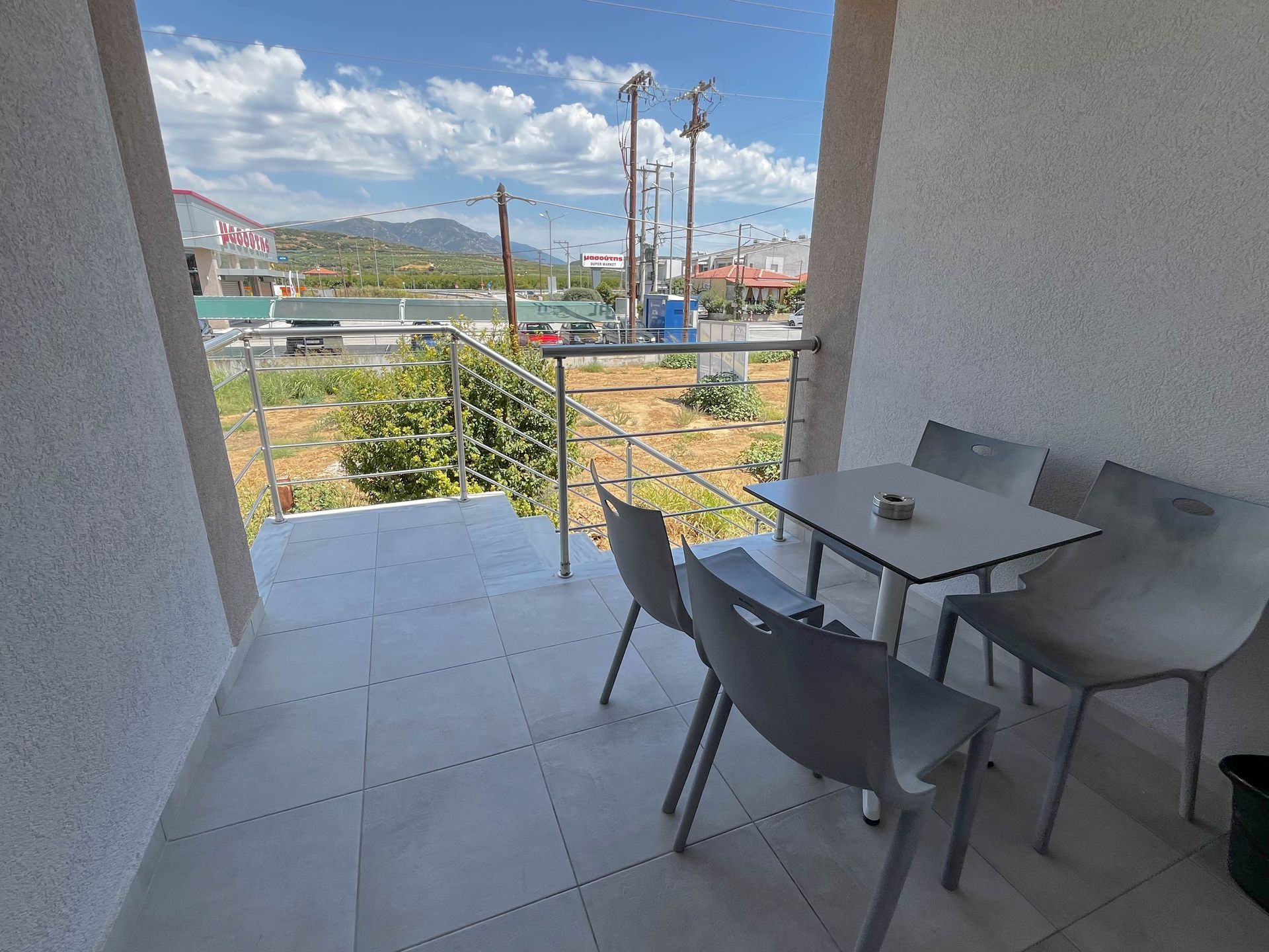 Balcony with table and chairs overlooking a street scene with mountains in the distance.