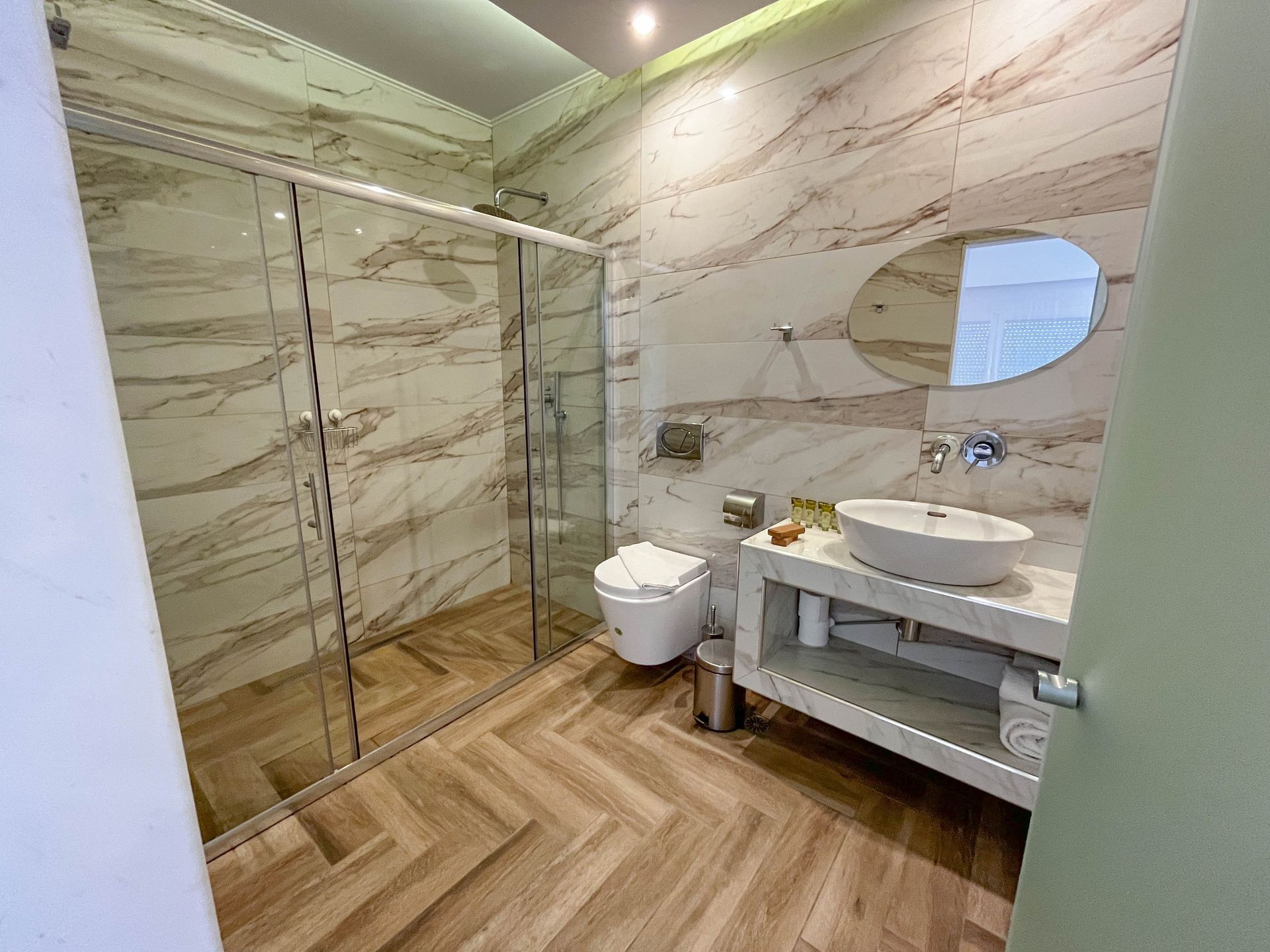 Modern bathroom with glass shower, floating sink, and marble-look walls and flooring.