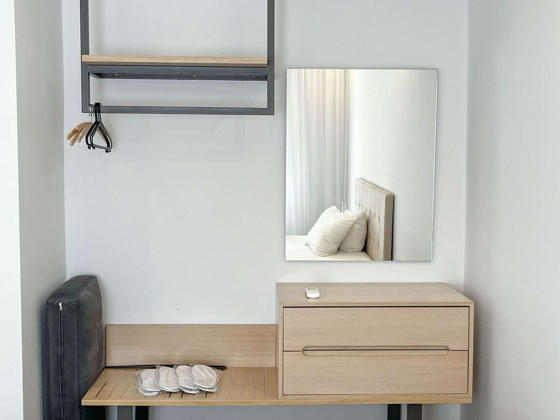 Bedroom corner with mirror, shelf, wooden drawers, bench, and clothing items.