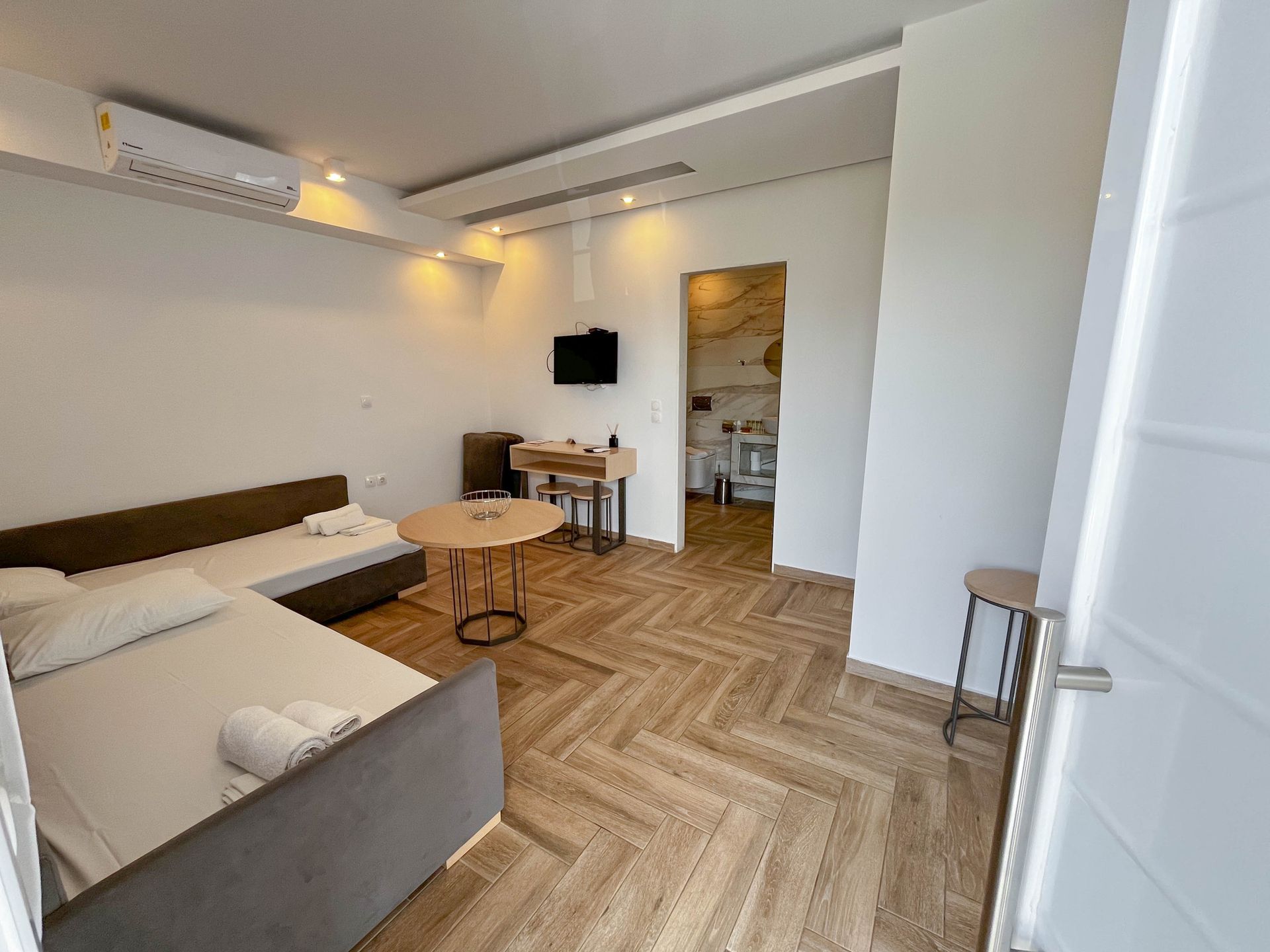 Modern studio apartment with sofa-bed, small table, TV, and open doorway to a bathroom.